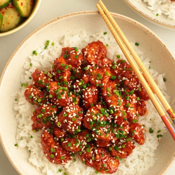 crispy Korean popcorn chicken bites in a bowl with rice, chives and sesame seeds
